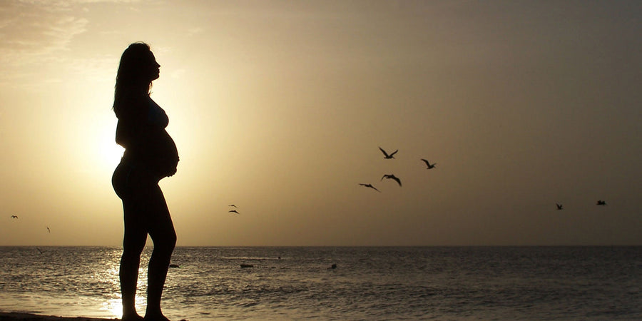 Mother holding her pregnant stomach at the beach taking prenatal vitamins during sunset
